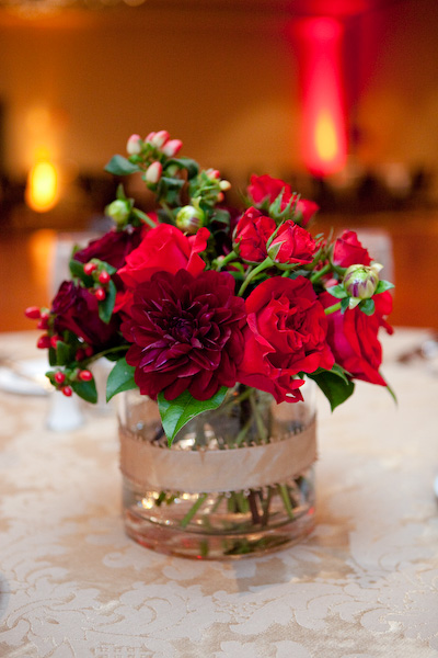 Low centerpieces of burgundy dahlias red roses and red hypericum berries 